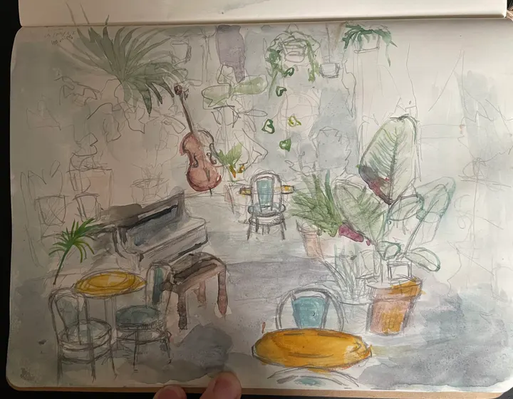 Watercolour and pencil sketch of a café filled with plants, a cello against the wall and yellow cushions on the seats