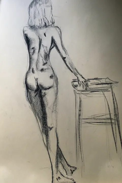 Charcoal life drawing of a standing nude figure leaning on a stool, seen from behind