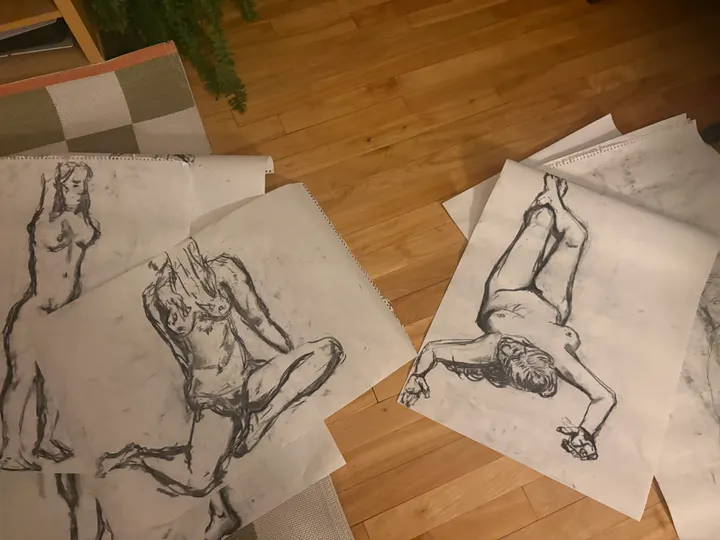 Several charcoal figure studies on loose sheets, spread across a wooden floor