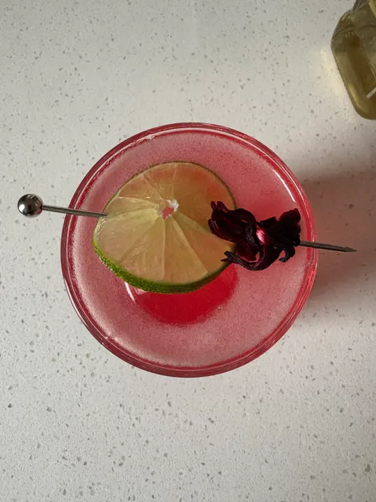 Overhead view of a pink drink with a lime wheel and a hibiscus flower on a pick