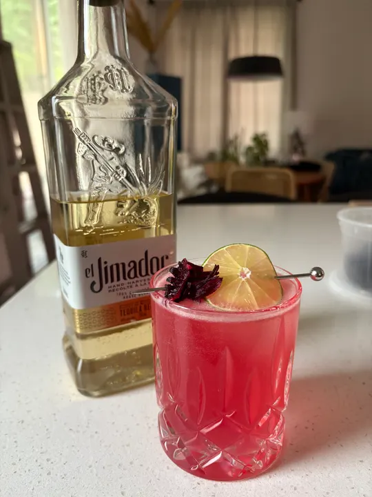 The pink hibiscus drink beside a bottle of tequila