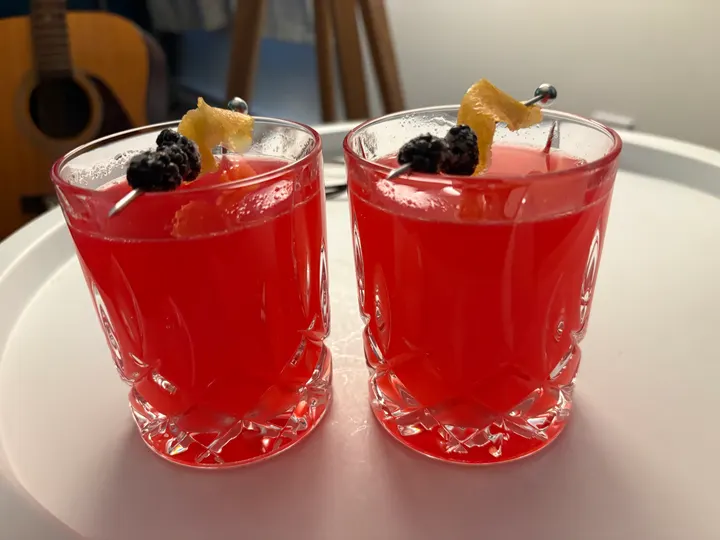 Two red drinks in cut-glass tumblers, each topped with a blackberry and lemon
