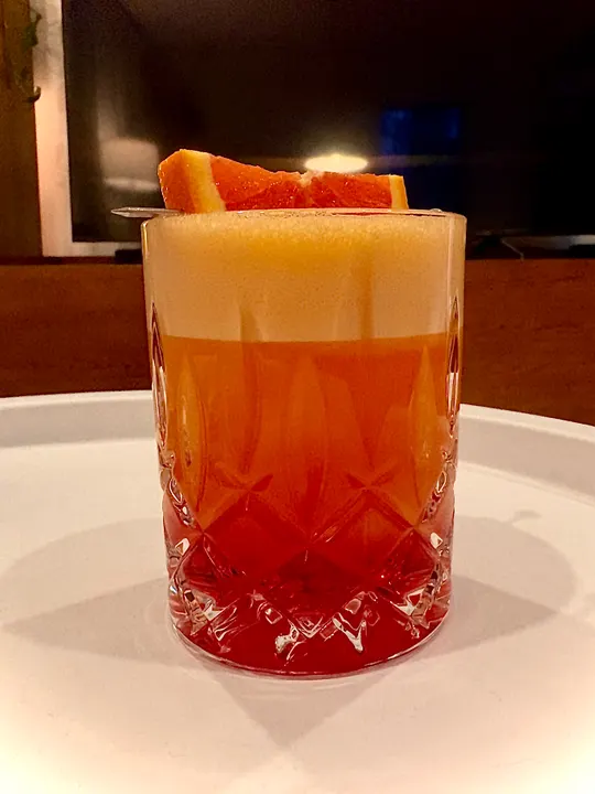 Layered orange and red drink in a cut-glass tumbler, topped with an orange slice