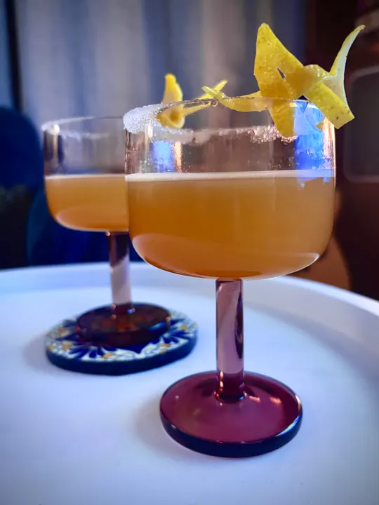 Two golden sours in stemmed glasses with lemon twists