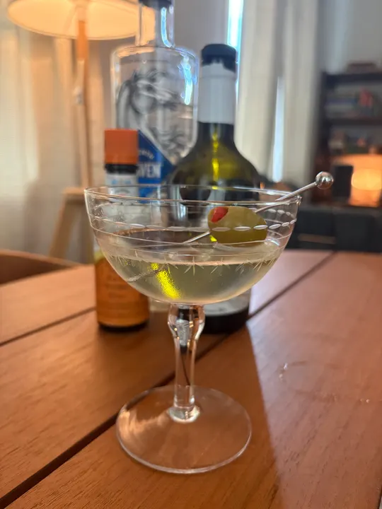 Martini in a cut-glass coupe with an olive on a pick, bottles behind it