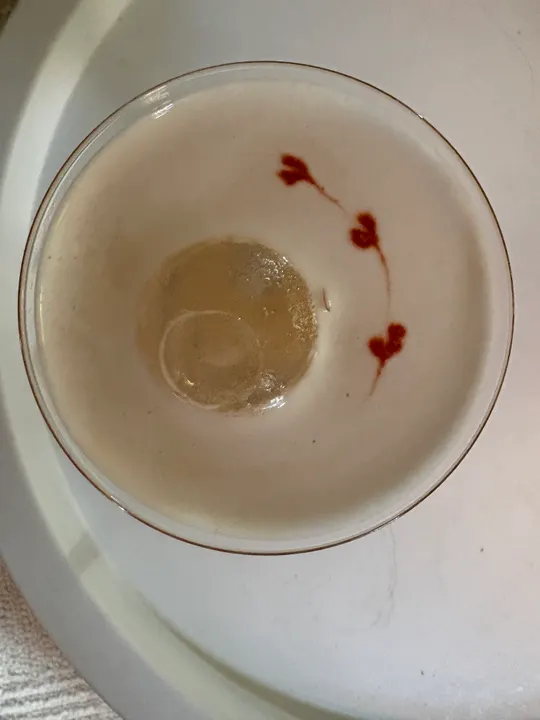 Overhead view of a sour with a clear ice sphere and drops of bitters drawn into hearts