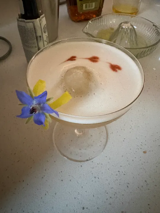 The sour garnished with a lemon twist and a blue borage flower