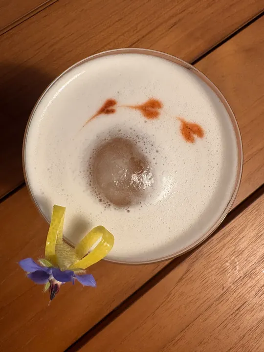 Overhead view of the finished sour: ice sphere, bitters hearts, borage and lemon twist