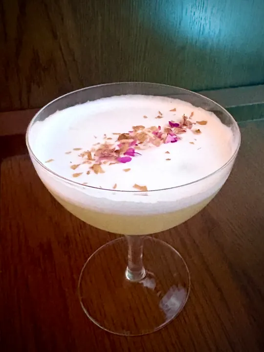 Frothy sour in a coupe, scattered with dried rose petals
