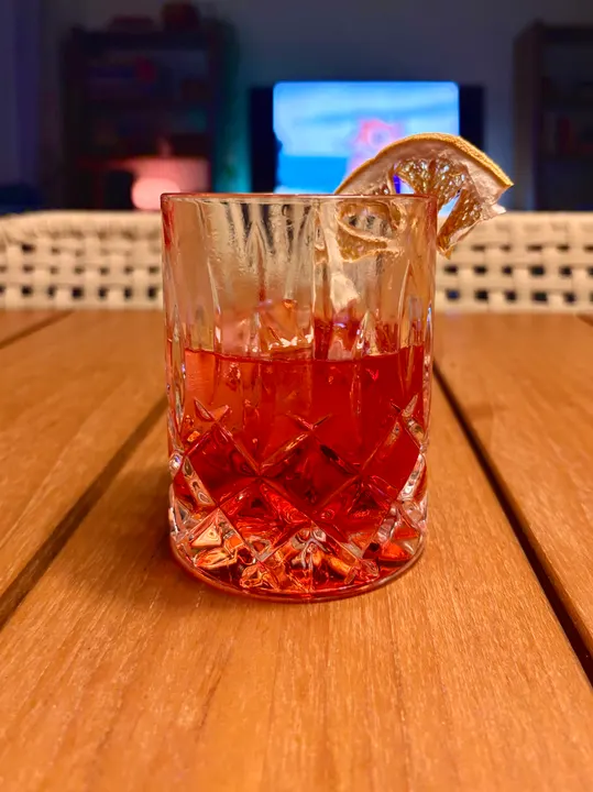 A red cocktail in a rocks glass with a dried citrus garnish