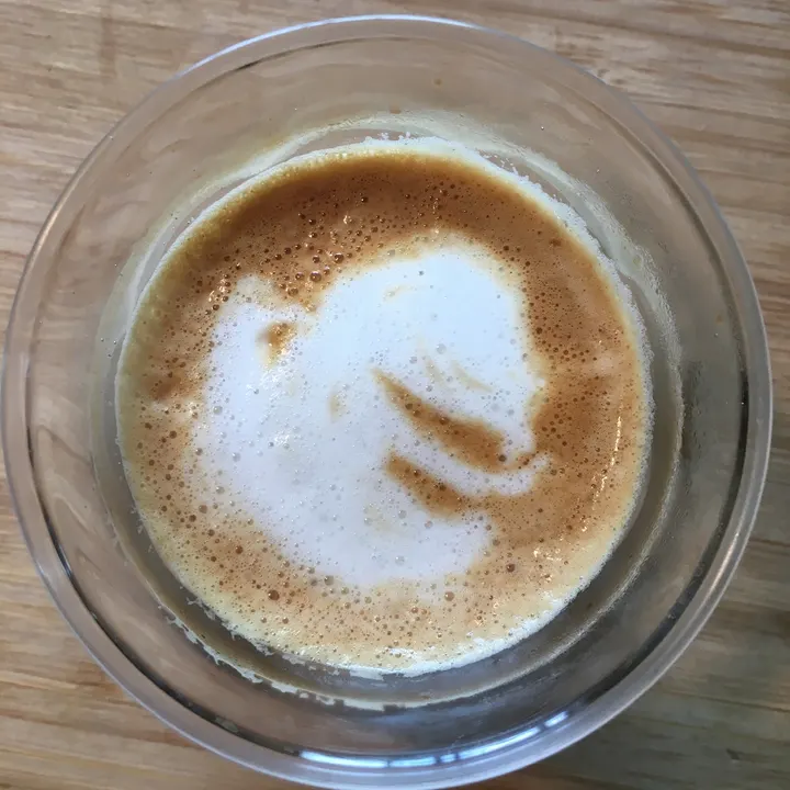 A white smudge drifting off to one side of a latte in a glass