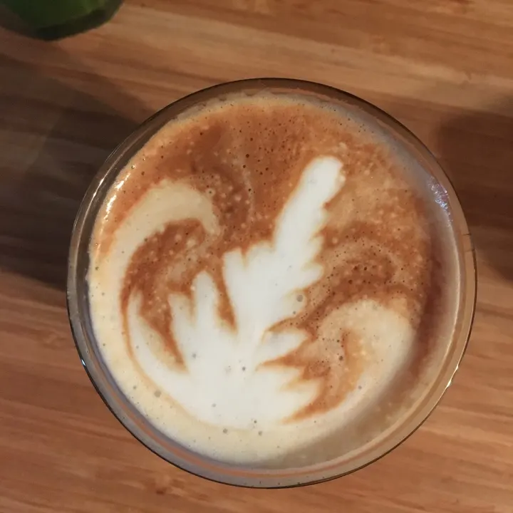 A rosetta swirling off to one side, in a glass on a wooden counter