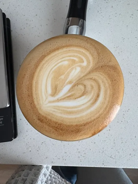 A heart swirled sideways, a portafilter handle beside the cup