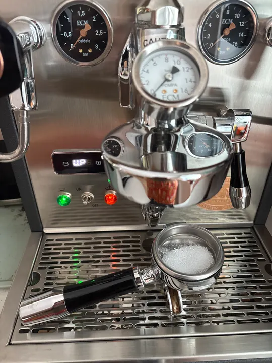 Close-up of the espresso machine group head, its pressure gauges and a portafilter resting on the drip tray