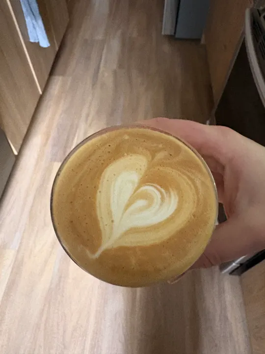 Hand holding a latte over a wooden floor, a crisp heart on top