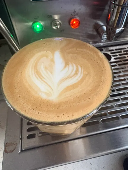A rosetta in a glass on the drip tray, the machine’s lights behind it