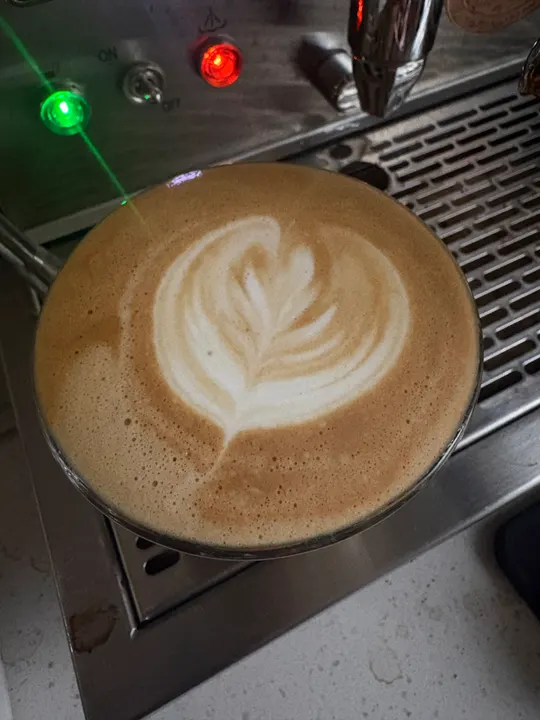 A latte on the drip tray with a full, well-defined rosetta