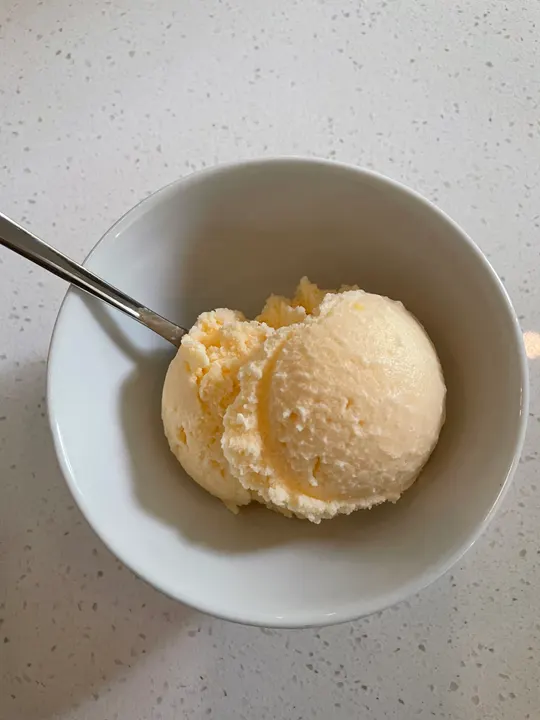 Two scoops of pale yellow ice cream in a white bowl