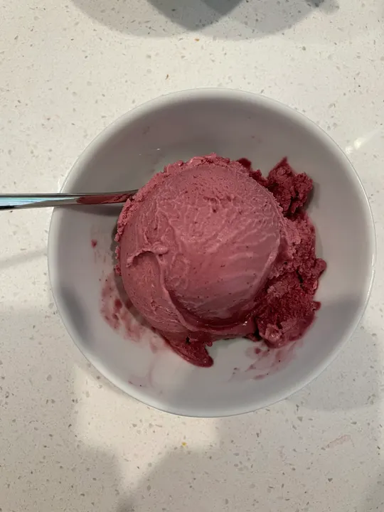 A scoop of deep pink berry-coloured ice cream in a white bowl