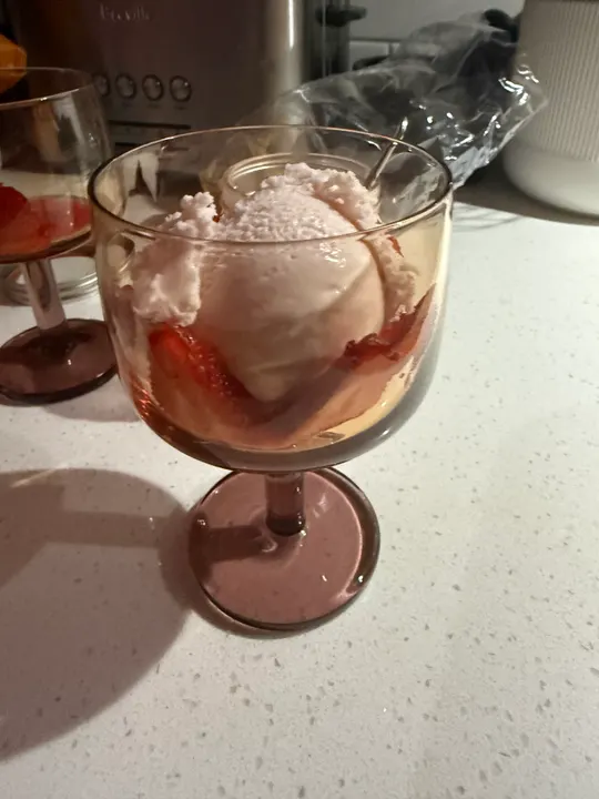 A scoop of pale pink strawberry ice cream on sliced strawberries in a stemmed glass