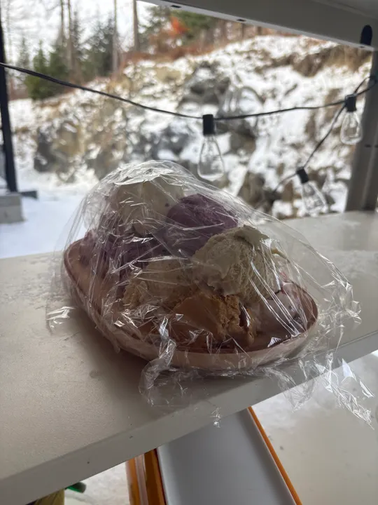 Scoops of purple and beige ice cream under cling film, set outside in the snow